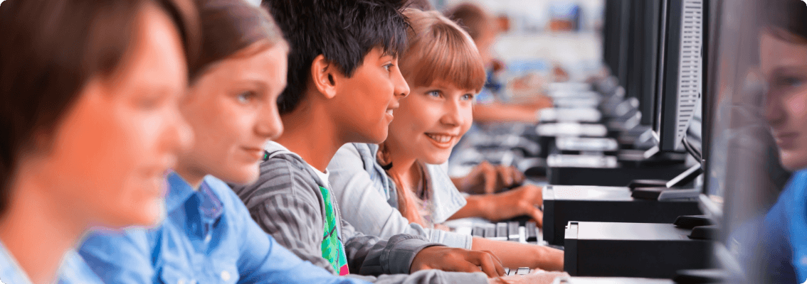 Foto de quatro crianças olhando cada uma para uma tela de computador sorrindo
