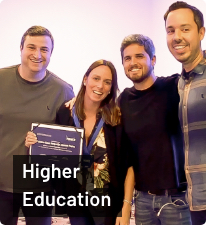 Da esquerda para direita: Junior Borneli, mulher participante do Power Class, Rony Meisler e Gustavo Caetano; todos de pé e sorrindo; texto 'Higher Education' abaixo